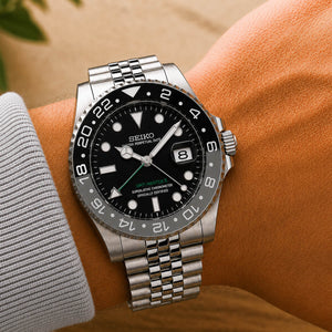 Seiko Bruce Wayne GMT automatic mod watch with black and gray bezel and jubilee bracelet on mans hand