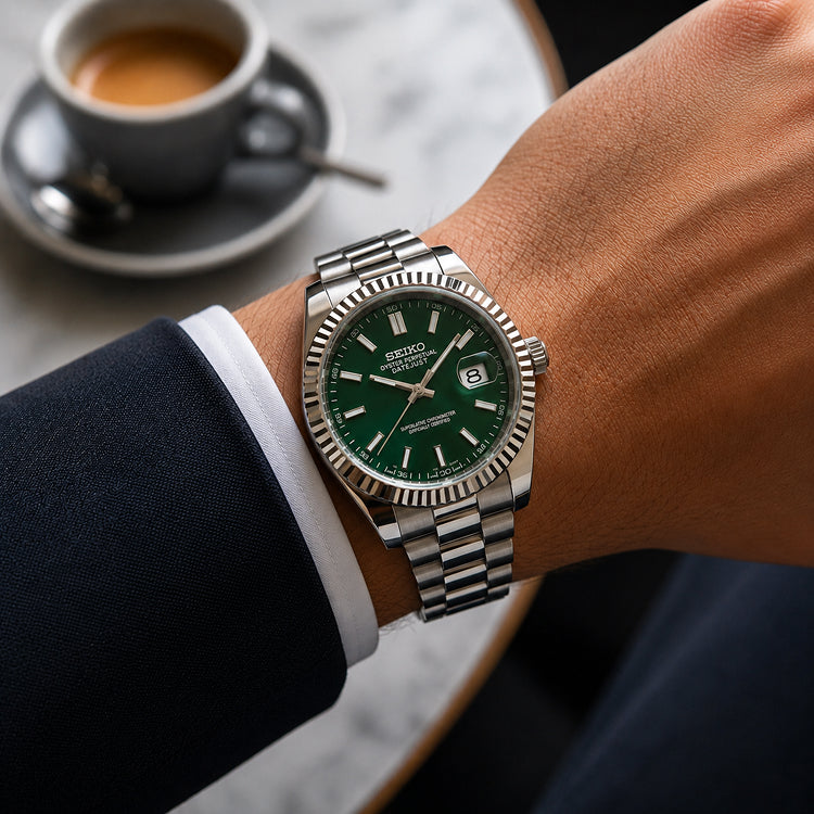 A wrist wearing a Seiko Prospex stainless steel watch with a green dial and fluted bezel, shown in a lifestyle setting with a coffee cup on a table in the background.
