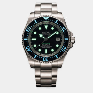 A Seiko Prospero Sea-Dweller wristwatch with a stainless steel bracelet, featuring a black dial with bright green luminescent markers and a black bezel with a blue 60-minute subdial.